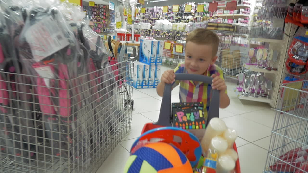 niño feliz en el centro comercial con un carrito lleno de cosas de fiesta