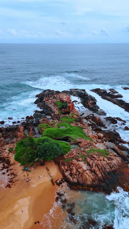 sandy beach with rocks and waves of the ocean splashing by boulders. indian ocean waterscape at backdrop. vertical video.