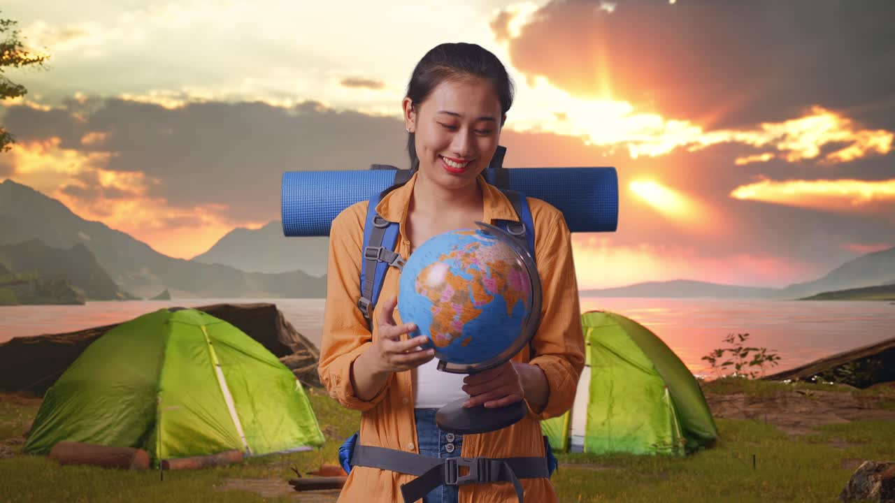Woman looking at a globe while camping at sunset