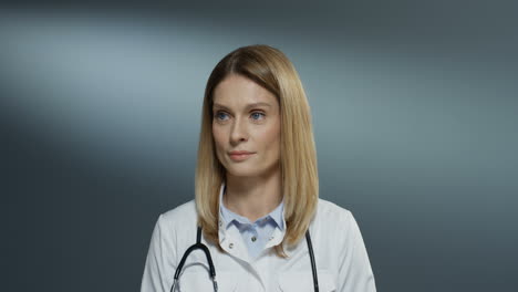 pretty young female medic in white gown and with stethoscope on her neck smiling joyfully to the camera