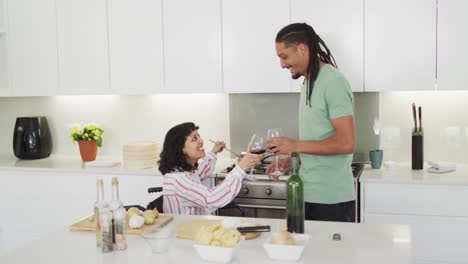 happy biracial woman in wheelchair preparing food and drinking wine with male partner in kitchen