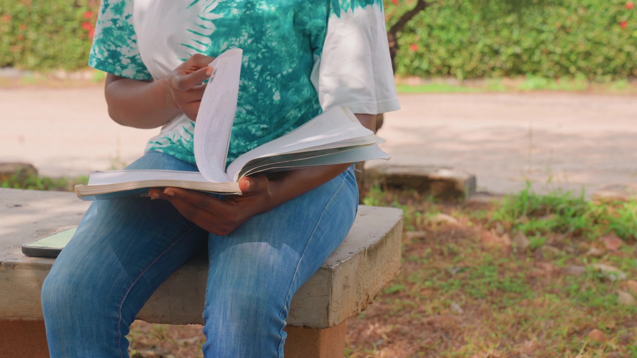 Mother journaling on park bench, flipping notebook pages and writing notes, casual denim jeans and green shirt, sunlit pathway and grass background, intimate closeup on hands, reflective parent moment