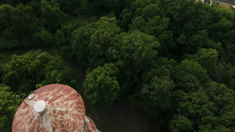 Bird's-eye-view-of-tree-tops-in-Fort-Harrison-park,-dolly-out-reveals-watertower