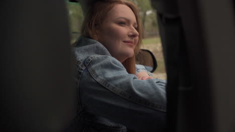 red haired woman enjoys a drive through the countryside from the window of the car