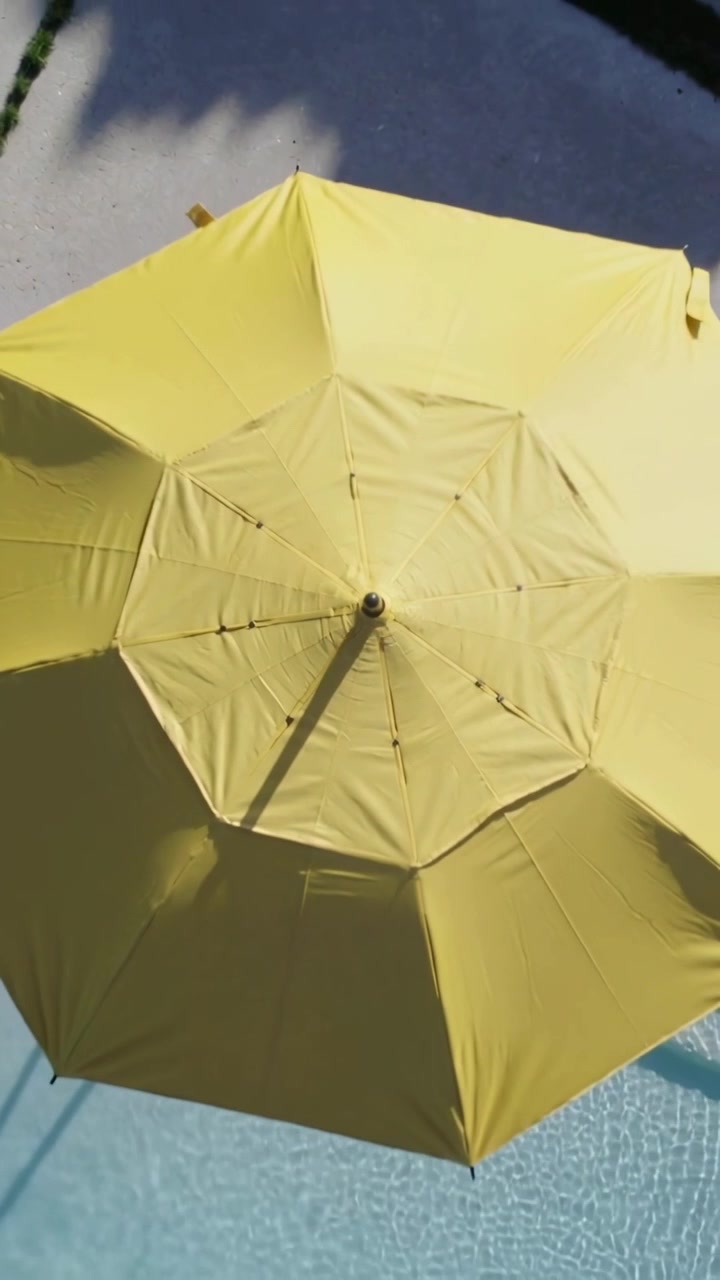 Video verticale: La telecamera si allontana, mostrando le stecche di un ombrellone giallo sopra il ponte, rivelando la piscina e l'ombra.