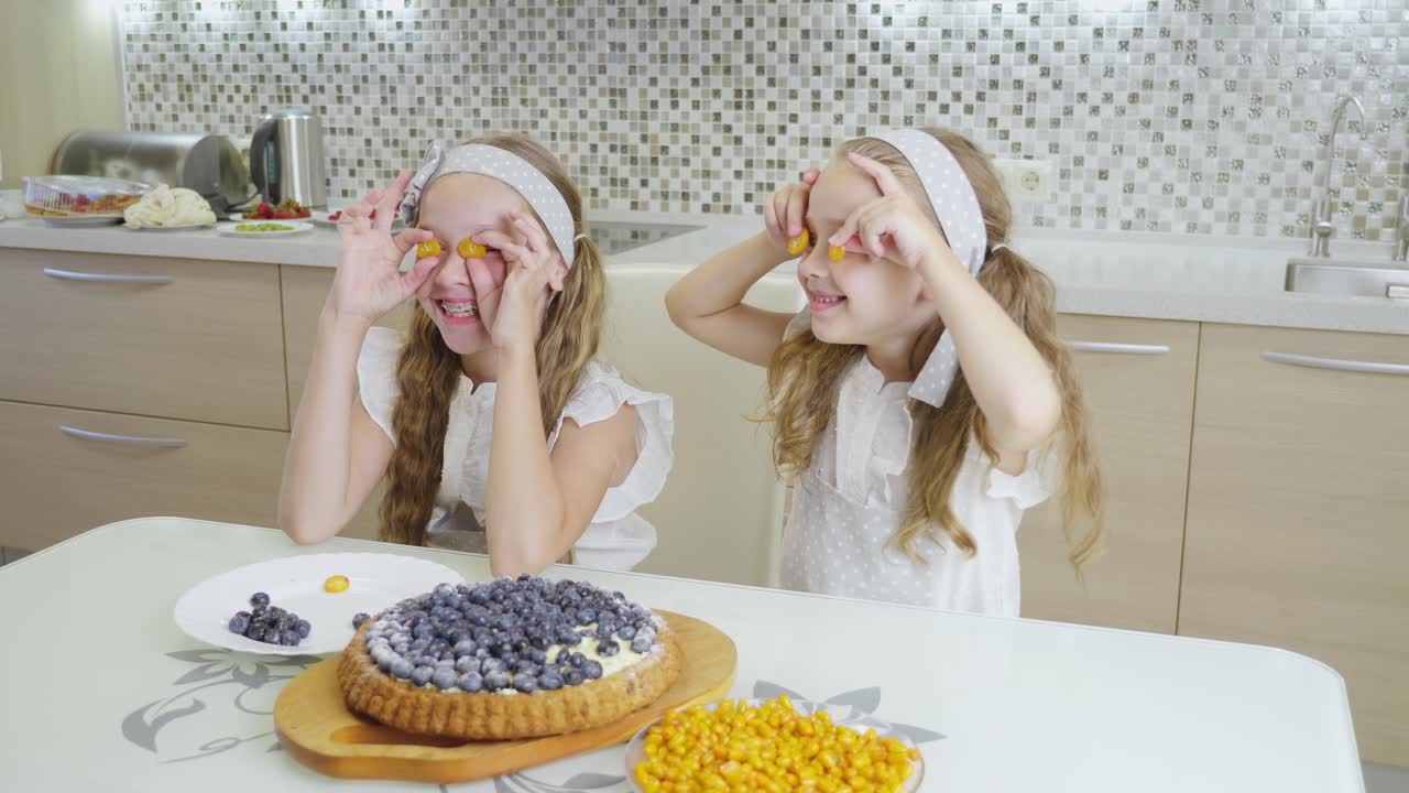 Twin girls having fun with a fruit tart in the kitchen