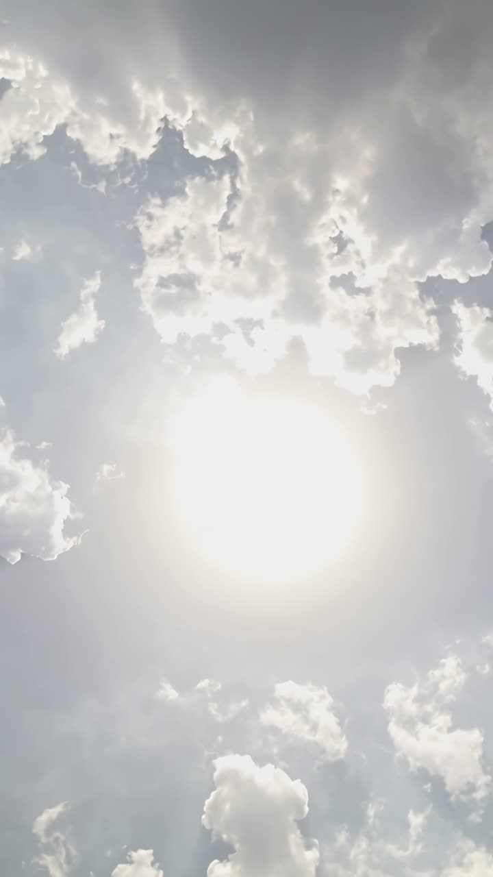 Vertical video: Filming sun with camera pointing upward capturing halo at noon sky, clouds drifting