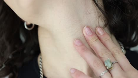 close-up of a person's hand touching their neck, adorned with jewelry