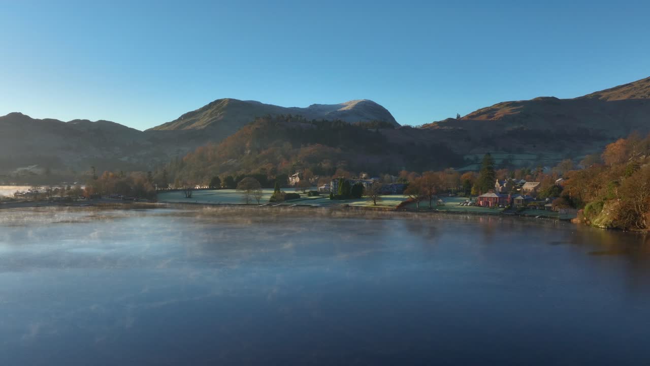 가을 새벽에 산으로 둘러싸인 호수 마을  ⁇ 에 있는 평온한 호수 표면에 천천히 굴러오는 안개