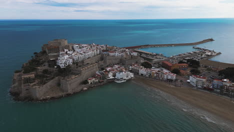 wide aerial over rocky coastline and stone castle of peniscola spain under blue sky