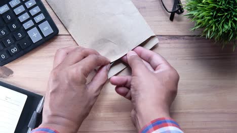 person placing money in brown envelope at desk.