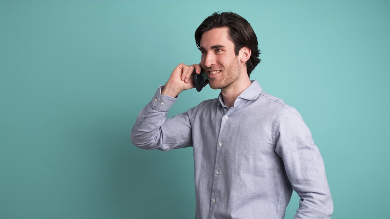 Smiling adult man talking on smartphone in blue studio