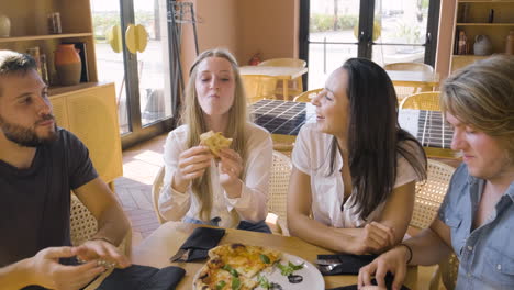 group of four happy friends sharing pizza and talking at restaurant