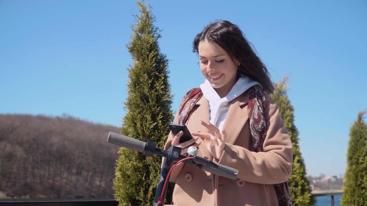 젊은 소녀는 휴대 전화 앱을 사용하여 전기 스쿠터를 임대합니다. 관광 전화 응용 프로그램. 젊은이와 비즈니스 사람들을위한 현대 기기