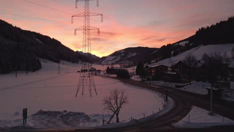 Aerial-shot-of-a-snow-covered-mountain-town,-winding-road-through-the-valley-during-sunset