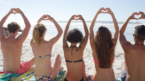 group of friends making heart shape gesture with their hands on the beach
