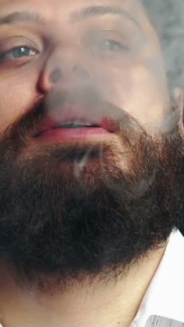 young smoker man relaxing. young bearded handsome man smoking cigarette while posing in studio vertical video