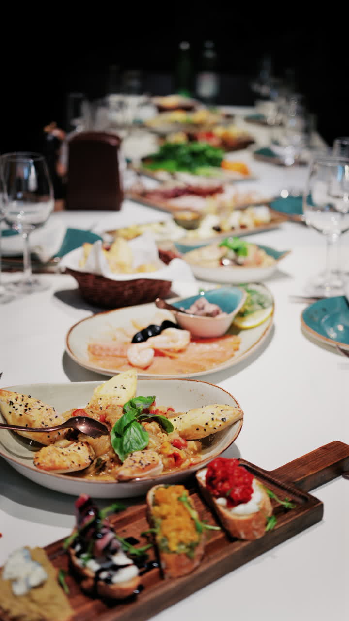 Overhead view of a restaurant table filled with gourmet appetizers, bread, seafood, and salads. Vertical