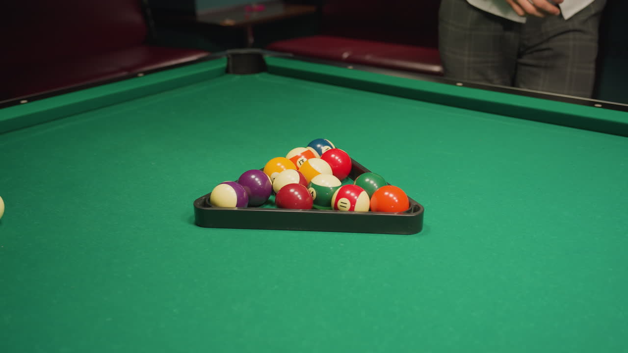 man's hand placing billiard balls into triangle rack on green pool table, preparing for game, action shot, close-up of hand, game setup, pool balls arrangement, focused sports moment