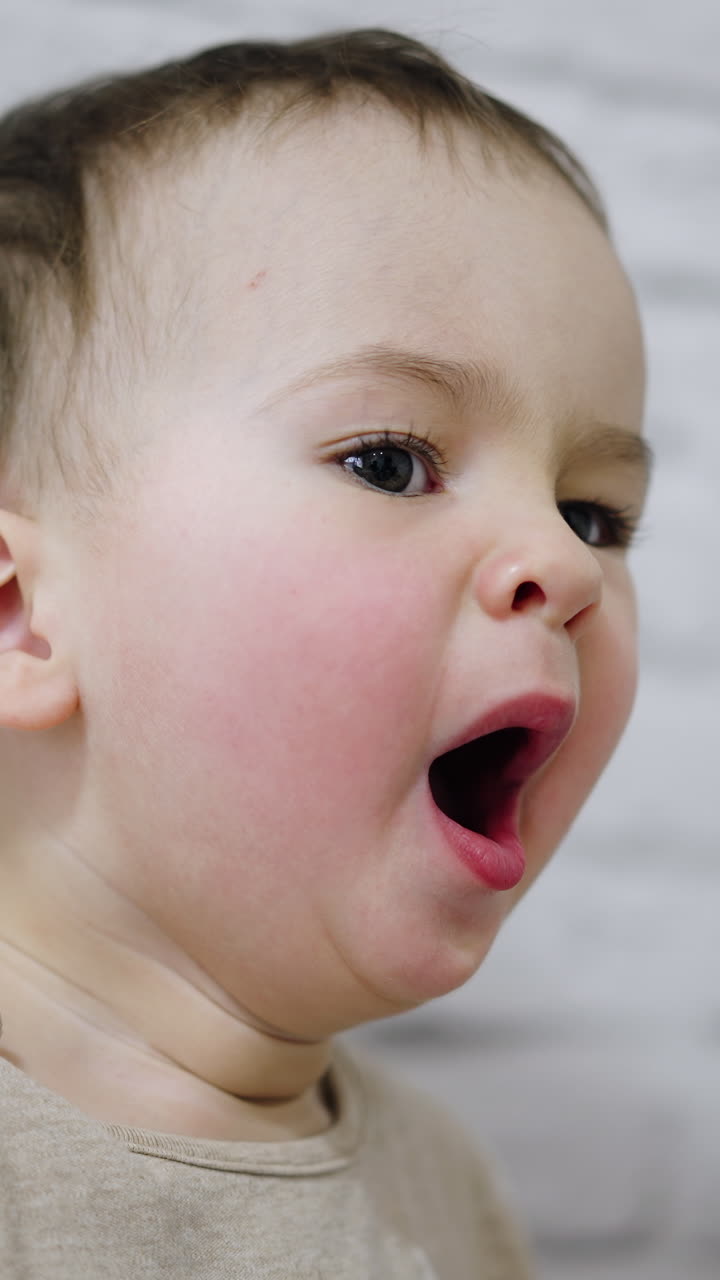 Charming baby boy with rosy cheeks yawning in front of camera. White backdrop. Vertical video