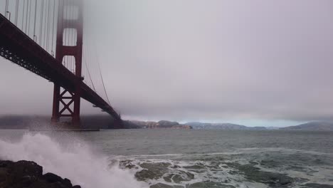 gimbal booming up shot from waves crashing into the rocky shoreline at fort point under the golden gate bridge on a stormy day in san francisco