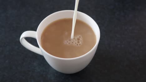 pouring milk into a steaming cup of coffee