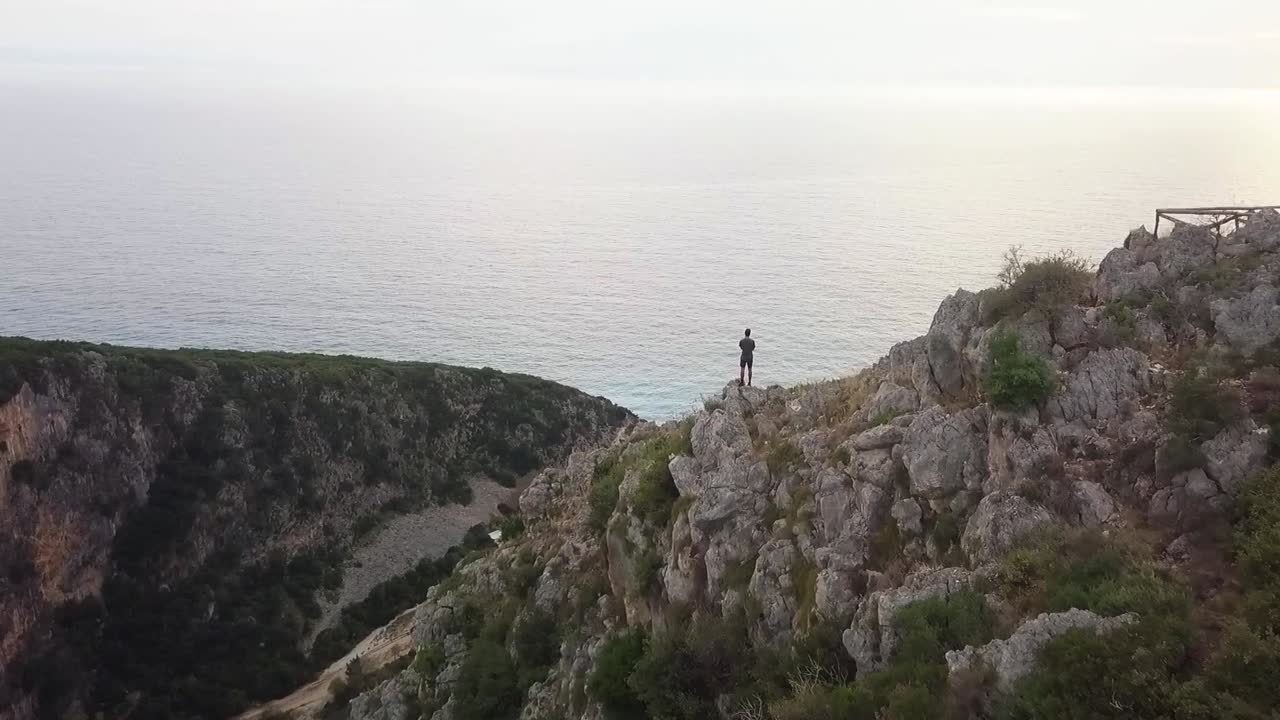 humano de pie sobre un enorme acantilado mirando hacia el océano al atardecer