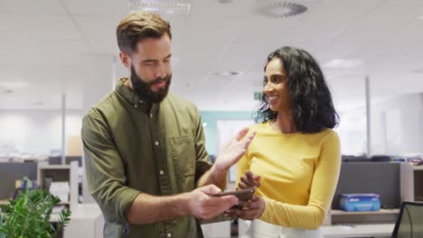 Video-of-happy-diverse-businesswoman-and-businessman-using-tablet-and-talking-in-office