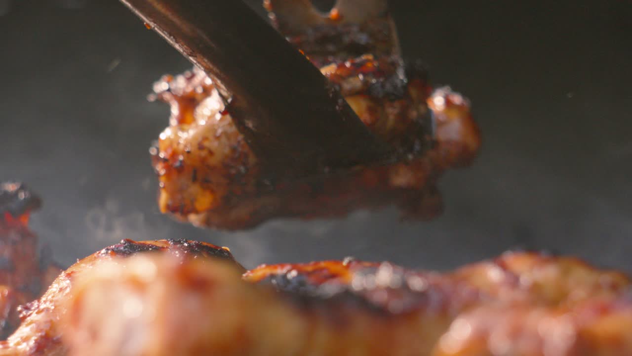 Smoke Rising Fast from Level View of BBQ with Crispy Skin Chicken Drumsticks Cooking with Chef Picking Up Pieces to Serve. High Protein Low Fat Lean Poultry Meat. Black Background with Copy Space.