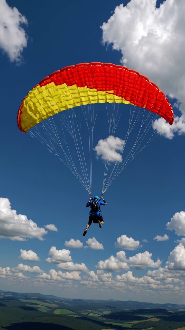 Aerial video shot of a paraglider with a red and yellow canopy soaring against a bright blue sky