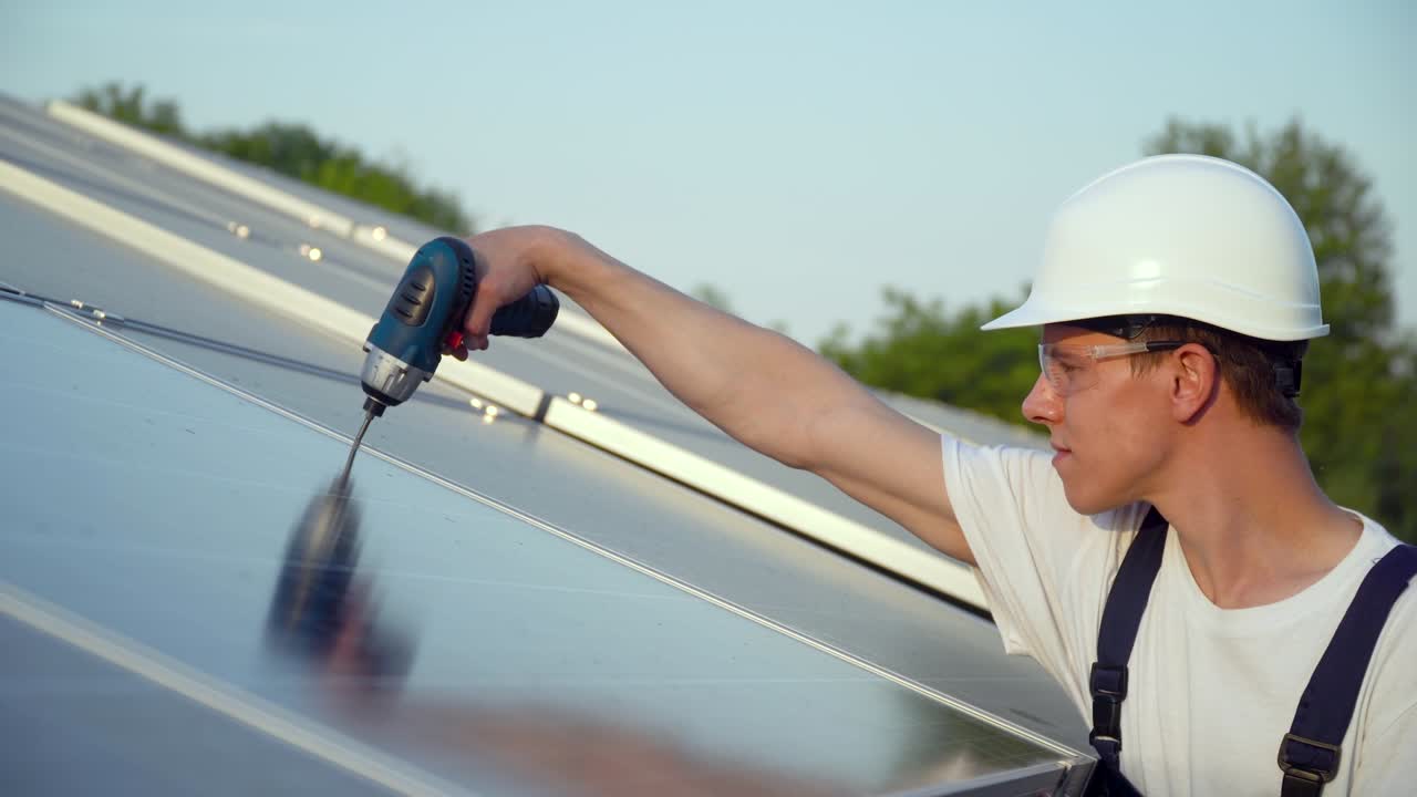 Young enginneer installing new sunny batteries. Worker in a uniform and hardhat installing photovoltaic panels on a solar farm