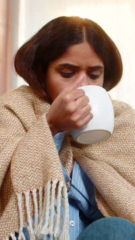 indian woman drinking hot tea and coughing at home under blanket showing cold and tired expression