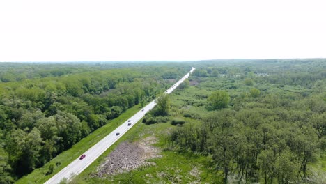 Toma-Aérea-De-Un-Camino-Rural-Que-Atraviesa-Un-Espeso-Bosque-En-Las-Llanuras