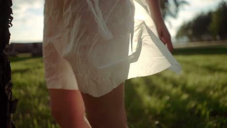 una mujer joven vestida con un vestido blanco transparente de pie contra la luz del sol en un campo por la noche