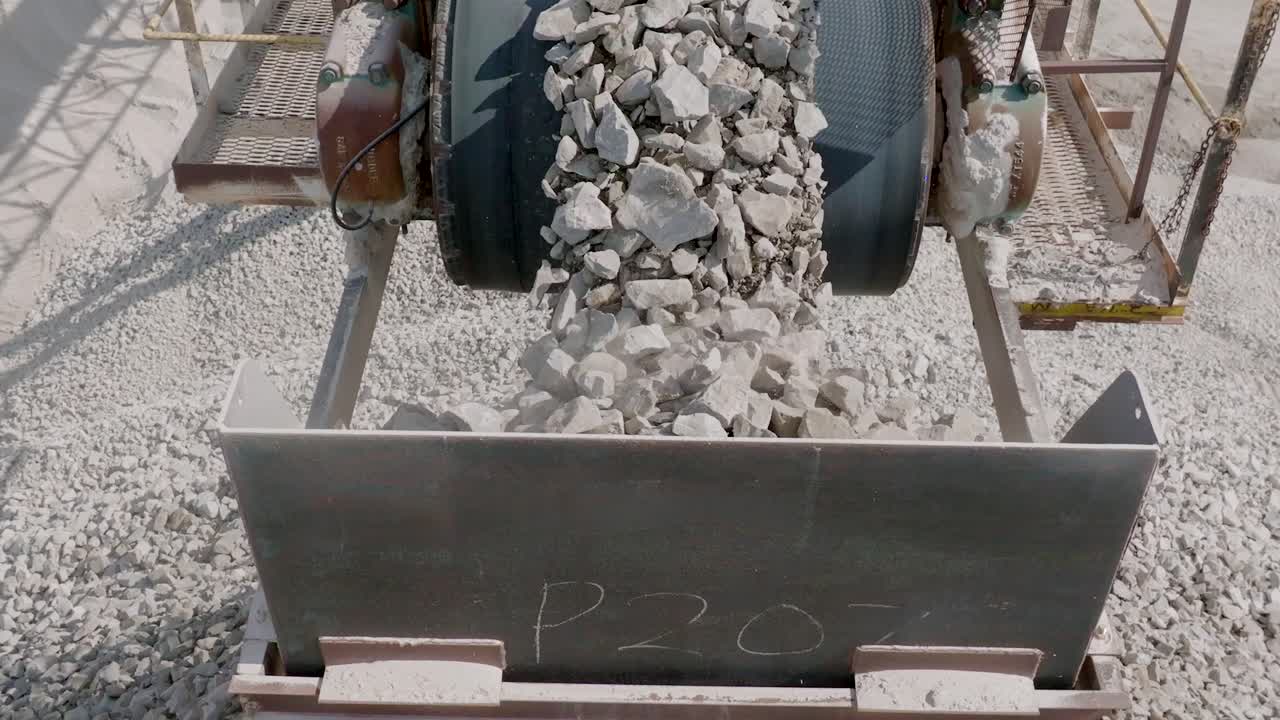 Slow motion footage of rocking piling up and falling off of a conveyor belt with the camera panning up to reveal more.