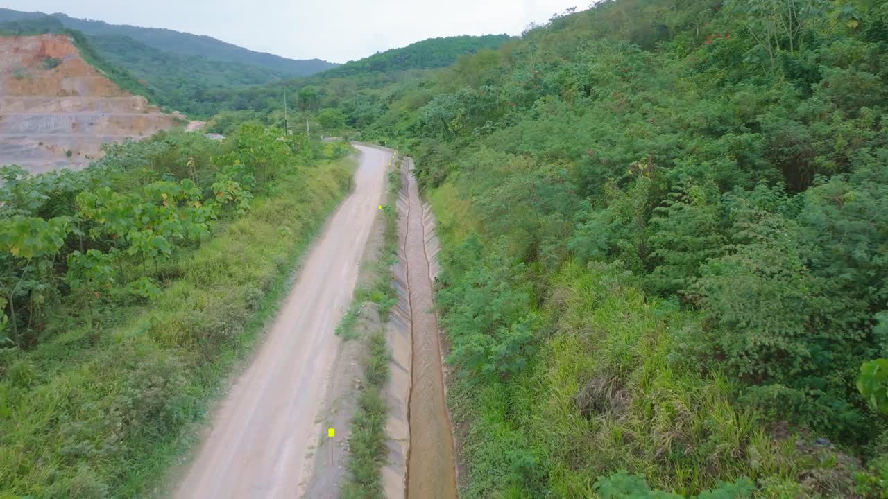 Dirt road through forest leading to open-pit mine for gold extraction, aerial