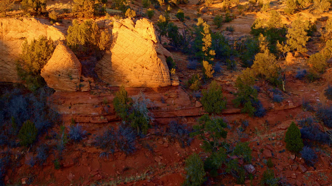 A slow aerial shot moves toward a stunning red rock arch, as the first rays of sunrise illuminate its rugged form.