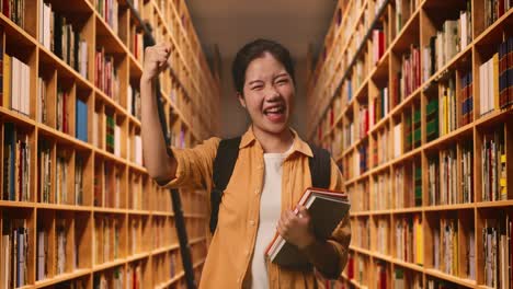 asian woman student with a backpack and some books screaming goal celebrating succeed learning in the library