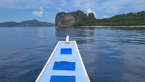 bow of boat sailing in front of uninhabited tropical island and beach