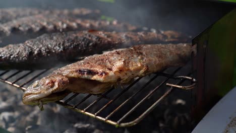 turning over grilled seasoned trouts on a smoking barbecue