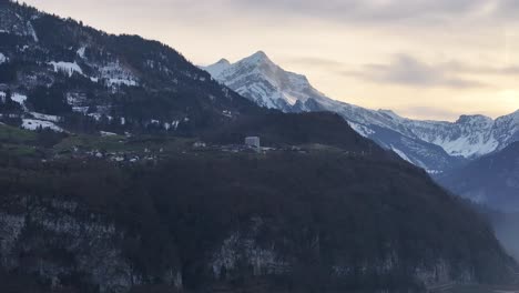 Eine-Drohnen-Luftaufnahme-Von-Filzbach-In-Der-Nähe-Von-Glarus,-Schweiz,-Zeigt-Die-Stadt-Umgeben-Von-Majestätischen-Schneebedeckten-Bergen-Und-Bewölktem-Himmel