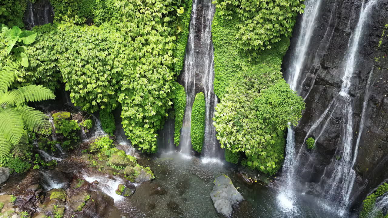 Pemandangan udara drone Kolam Air Terjun Banyumala di Buleleng, Bali. Beberapa air terjun mengalir ke cekungan alami yang tenang dikelilingi dedaunan hijau cerah dan hutan tropis