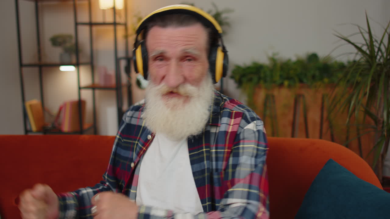 hombre feliz y relajado con auriculares inalámbricos bailando escuchando su música rock n roll favorita en el sofá de casa
