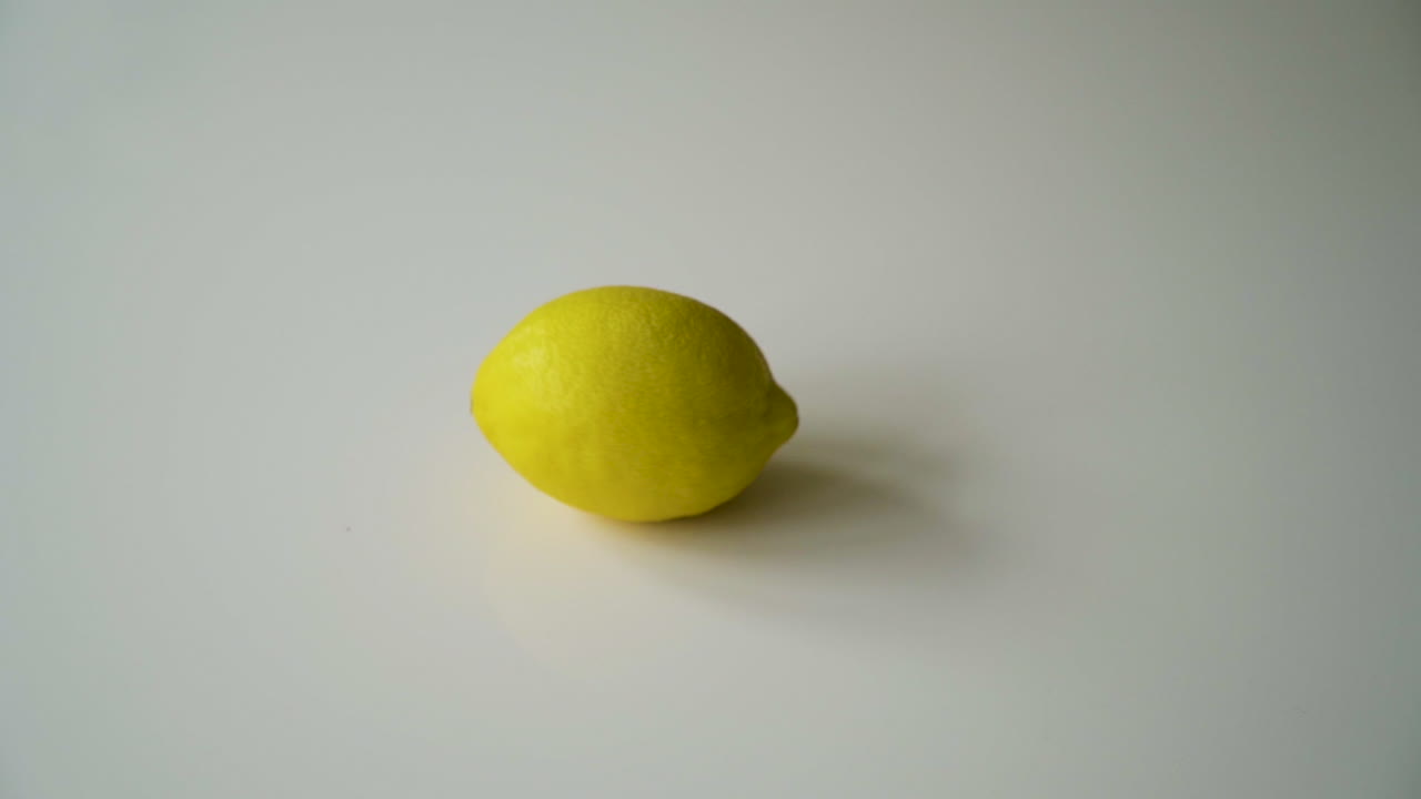 mano masculina girando un limón entero en cámara lenta sobre una mesa blanca con sombras y luego saca el limón de la mesa toma perfecta de texto de copia
