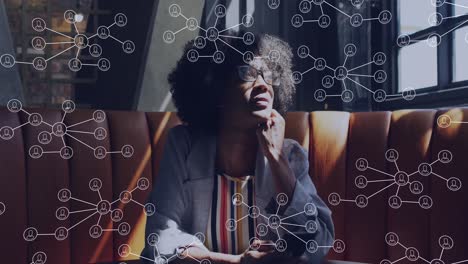 Animation-of-network-of-connections-with-icons-over-african-american-businesswoman-using-smartphone