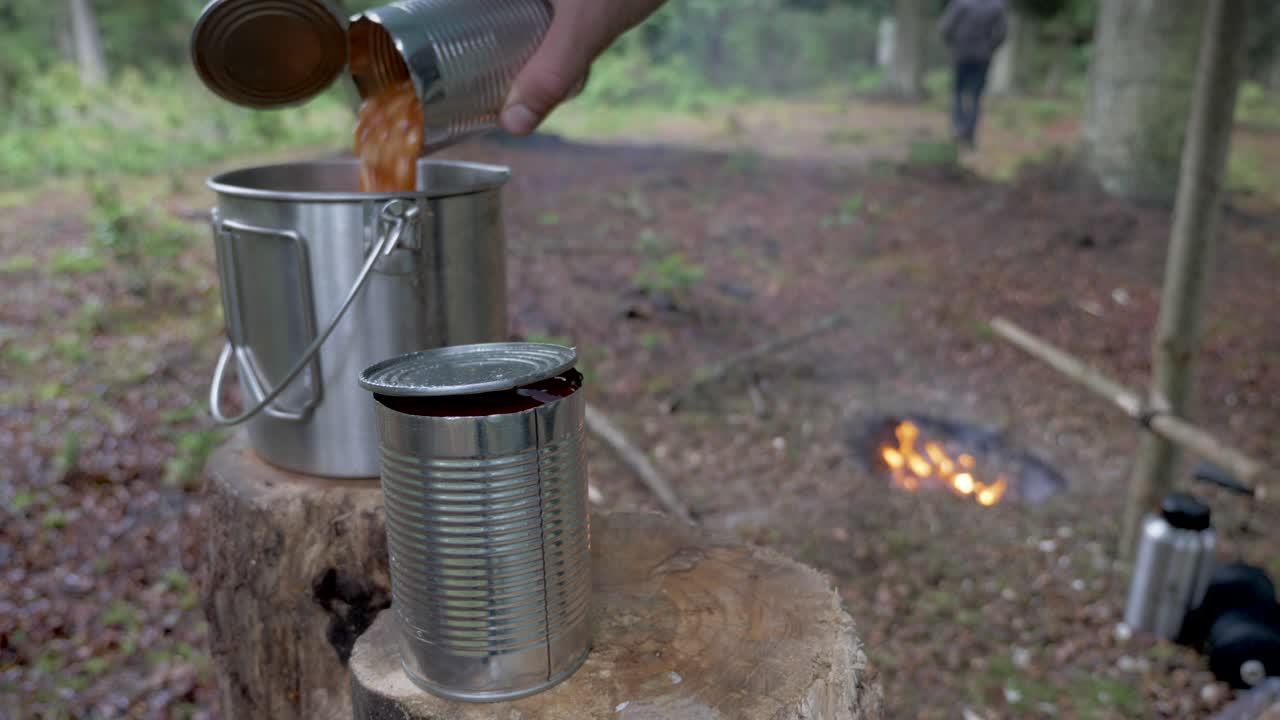 Male pouring baked beans into a pot in the forest, Static Shot