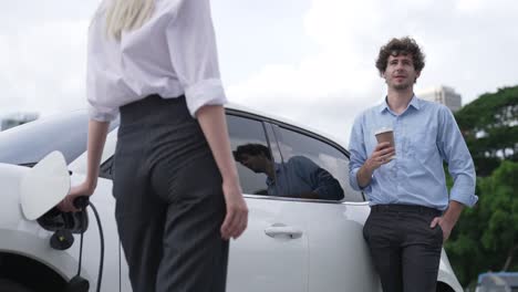 hombre de negocios y mujer de negocios progresistas apoyándose en el coche y el punto de carga.