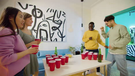 multiethnic young friends playing beer pong at home