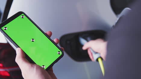 hombre cargando un vehículo eléctrico con un cable mirando una aplicación en su teléfono móvil