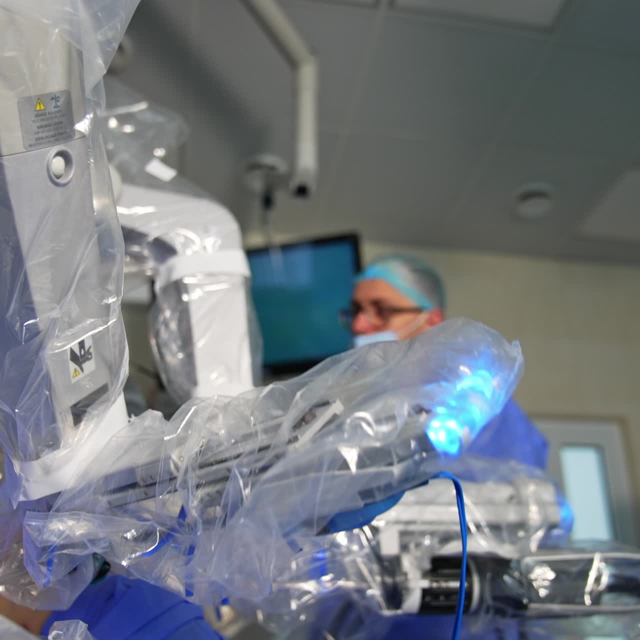 Robotic manipulator arm moves in the patient's belly. Minimal invasion operation conducted by machine. Doctor and nurse at backdrop